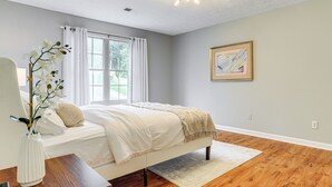 A bedroom with a bed, a window with curtains, a vase with flowers, a painting on the wall, and a ceiling light. - Walk to Dtwn Woodstock: Modern Home w/ Patio! (Woodstock)