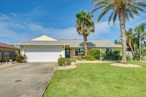 A single-story house with a garage, surrounded by a well-maintained lawn and palm trees.