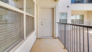 A corridor with a white door, large windows with blinds, and a balcony with a metal railing. - King Bed Fort Worth Home Near I-35W & DFW! (Crowley)