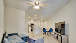 A modern living room with a sofa, coffee table, and a TV on a wooden cabinet. - King Bed Fort Worth Home Near I-35W & DFW! (Crowley)