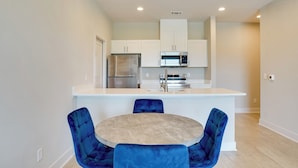Una cocina moderna con armarios blancos, electrodomésticos de acero inoxidable y una isla central con sillas azules.