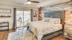 Ein Schlafzimmer mit einem großen Bett, einem Deckenventilator, einem hölzernen Kopfteil, einem Nachttisch, einem Sessel und Blick ins Freie.