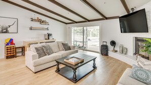 Ein Wohnzimmer mit Holzboden, einer Couch, einem Couchtisch, einem Kamin und einem an der Wand befestigten Fernseher.