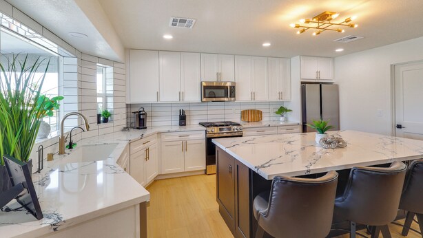 A modern kitchen with white cabinets, a central island with seating, stainless steel appliances, and a large window providing natural light. - 2 Mi to Windsor Beach! Updated, Sleek Family Home (Lake Havasu City)