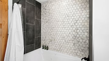 A bathroom with a white bathtub, dark tiles, and a hexagonal tile backsplash.