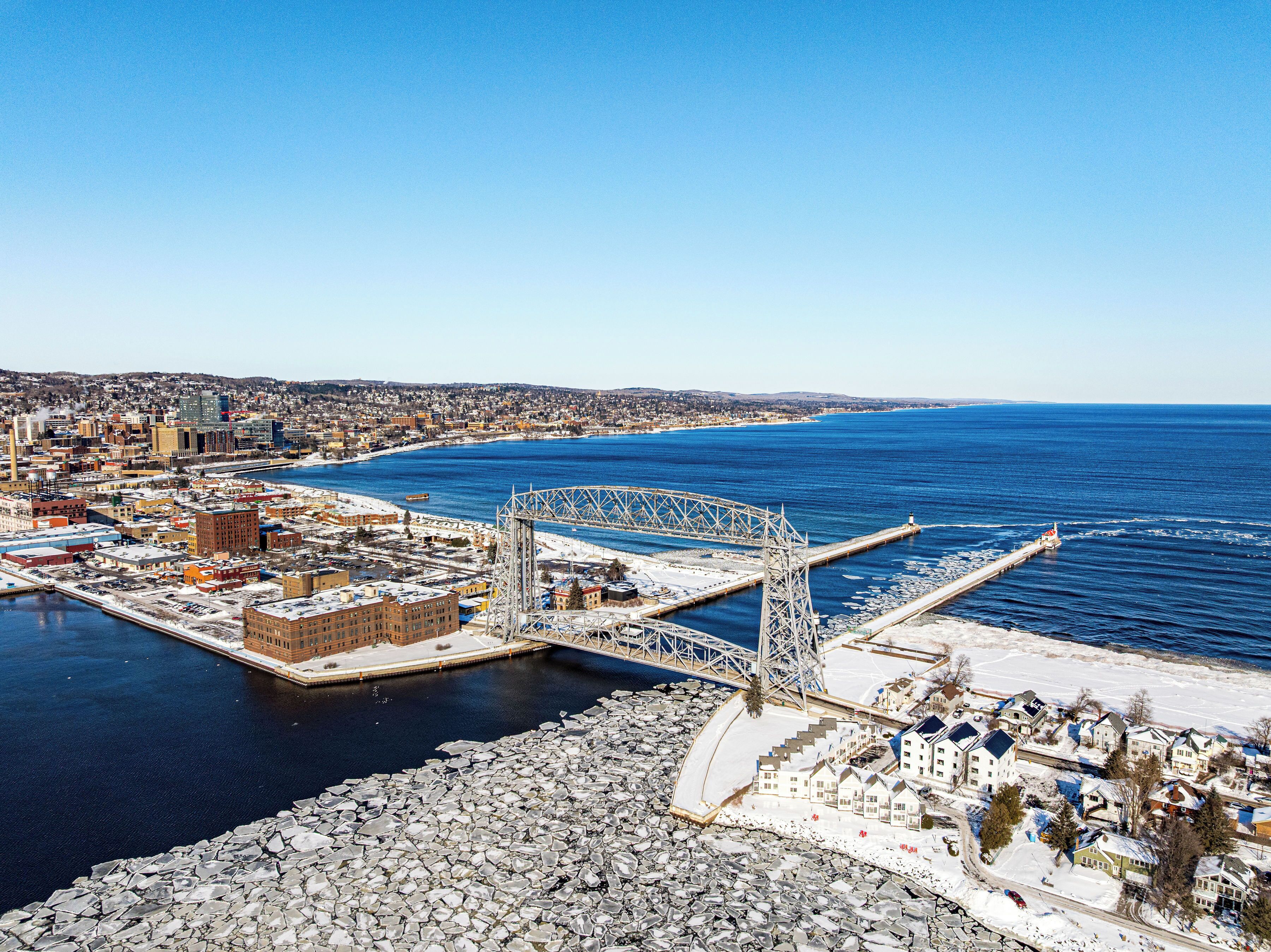 An aerial view of a coastal city with a prominent bridge, a marina, and residential areas.
