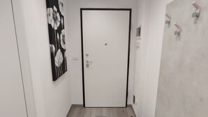 A room with a wooden floor, a white door, a black and white floral painting, and a white wall with a light fixture. - From Faith to the Sea Within walking distance of the sea, station and city center (Moneglia)