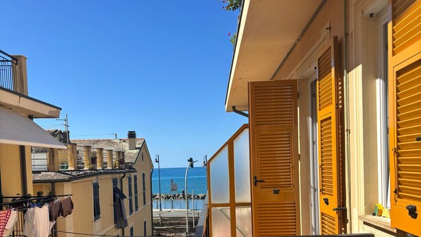 A narrow street with buildings on either side, a balcony with yellow shutters, and a view of the sea in the distance. - From Faith to the Sea Within walking distance of the sea, station and city center (Moneglia)