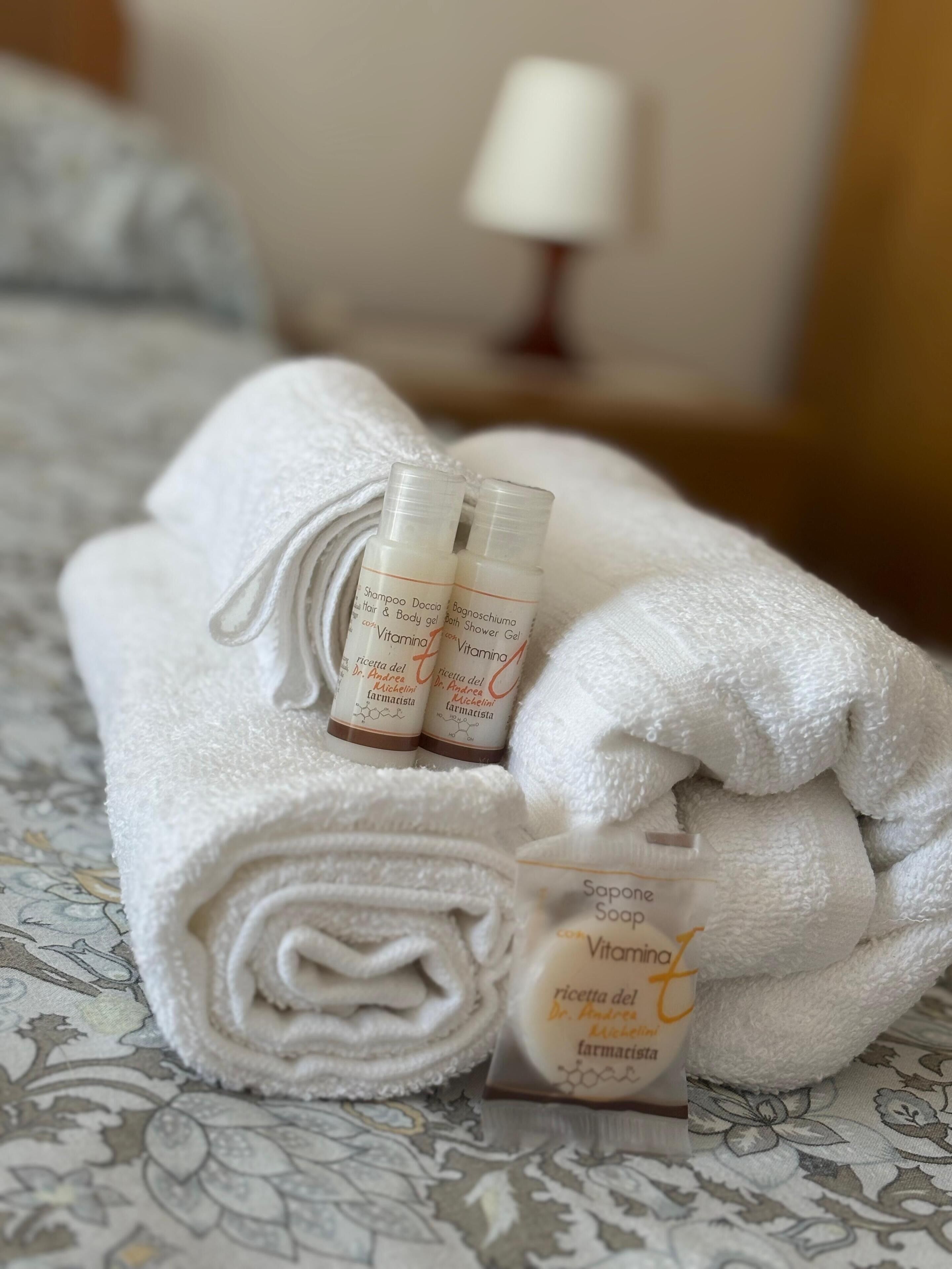 Ein ordentlich gefaltetes weißes Handtuch mit zwei Flaschen Shampoo und Seife auf einer gemusterten Bettdecke.