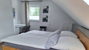 A bedroom with a wooden bed, a desk, a chair, and a window with curtains.