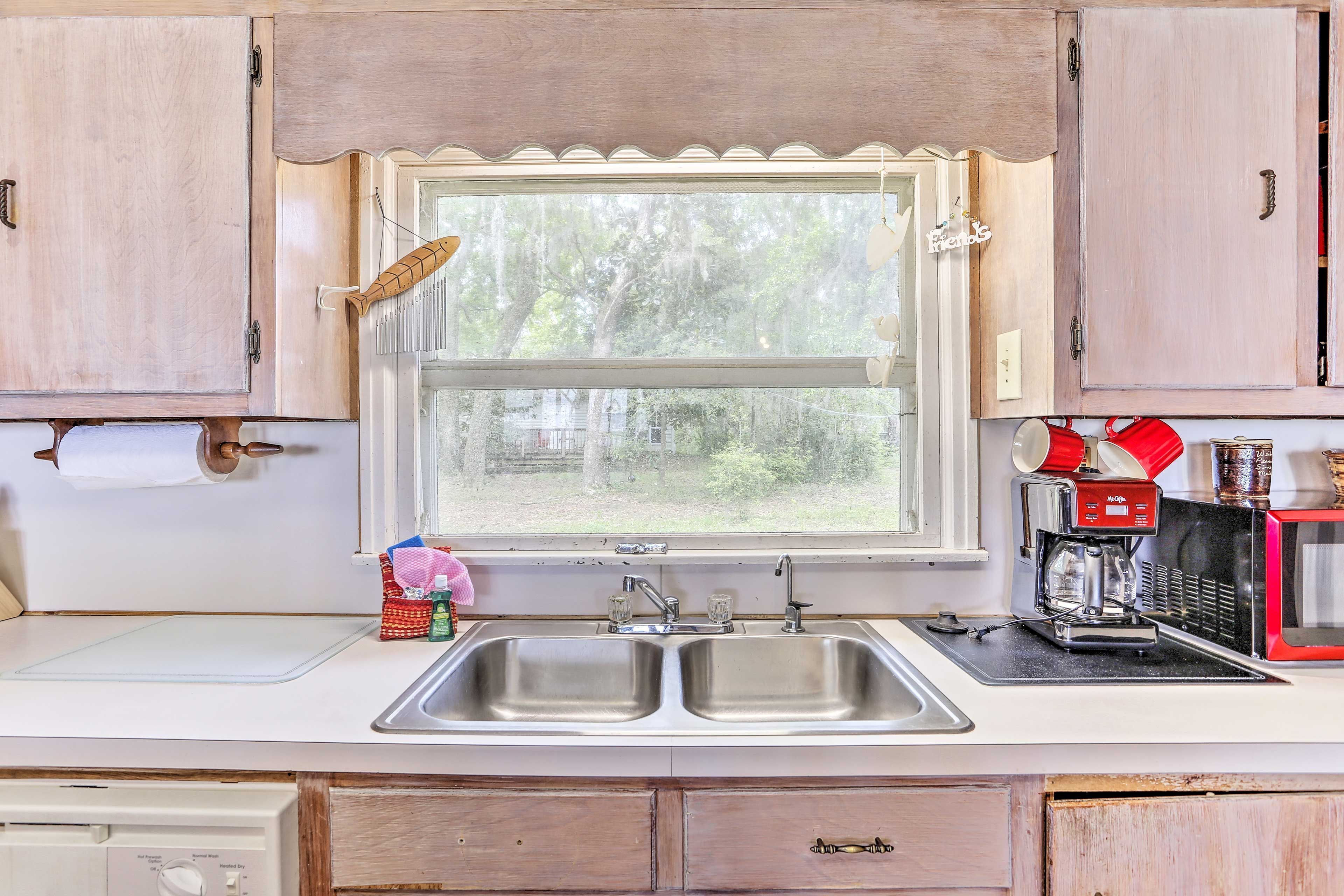 A kitchen with a double sink, a window with a view of trees, and a coffee maker on the counter.
