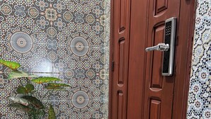Une porte en bois dotée d’un clavier pour l’ouverture, une plante en pot aux feuilles décorées et un mur recouvert de carreaux formant un motif géométrique.