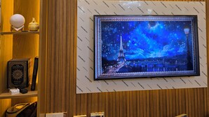 Un hall d’accueil d’hôtel doté d’un grand téléviseur à écran plat diffusant une image nocturne de la Tour Eiffel, de lambris en bois sur les murs, ainsi que de divers livres et objets décoratifs disposés sur des étagères.