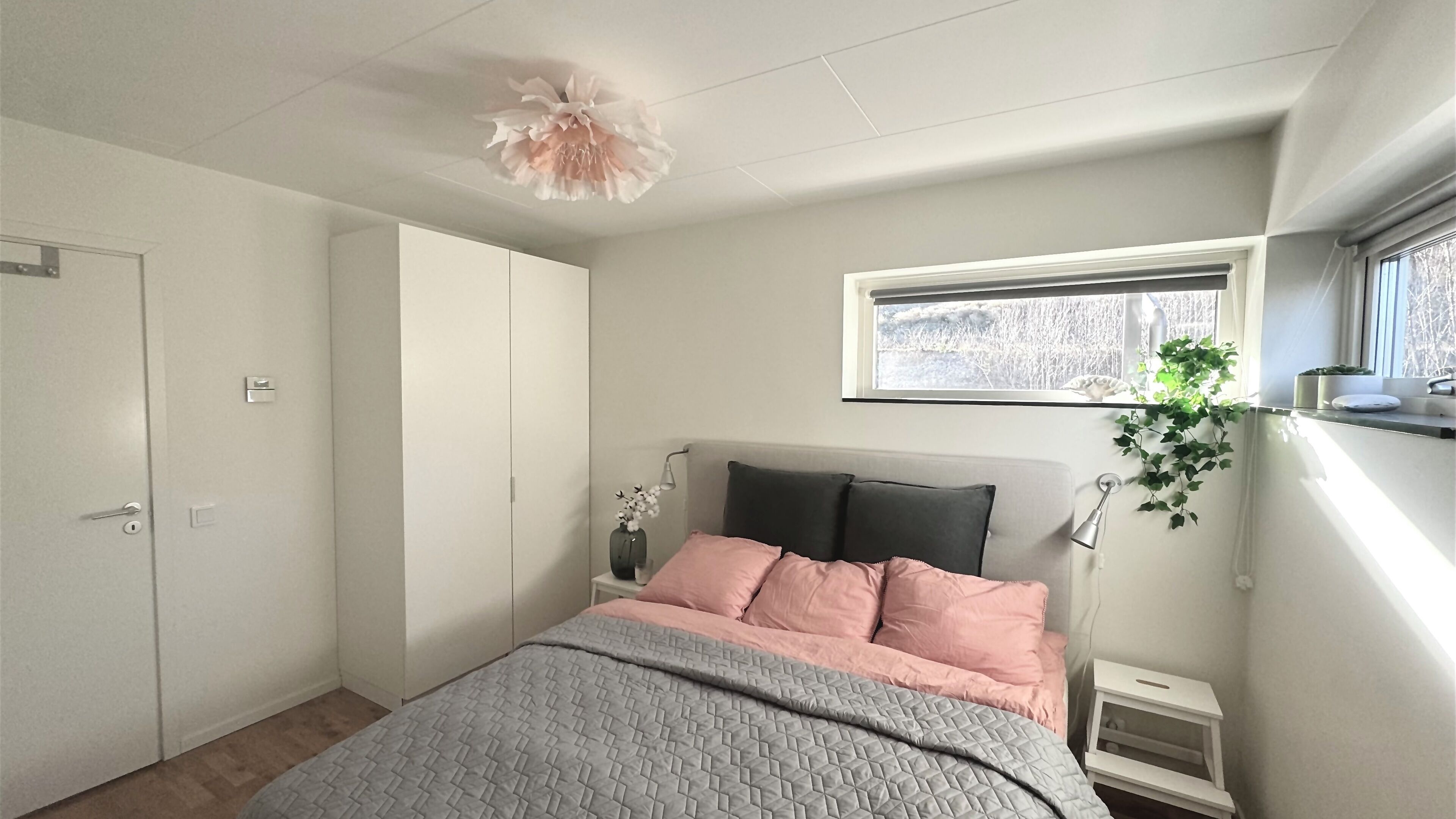 A bedroom with a bed, a window, a plant, and a wardrobe.