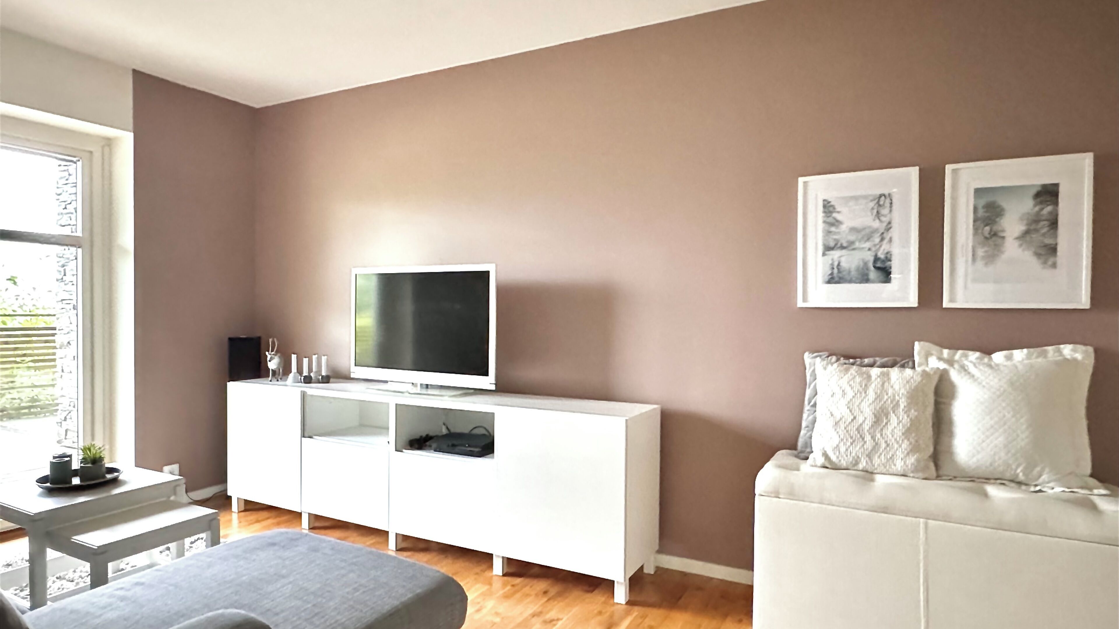 Un soggiorno con un mobile TV bianco, una TV a schermo piatto, un divano bianco e due quadri appesi al muro.