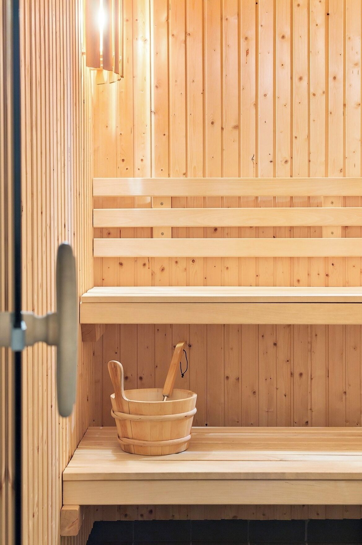 Eine Holzbank in der Sauna, mit einem Holzbecken und einem Holzlöffel.