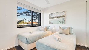 Slaapkamer met twee bedden, een groot raam met uitzicht op bomen en gebouwen, en een lijst met een afbeelding aan de muur.