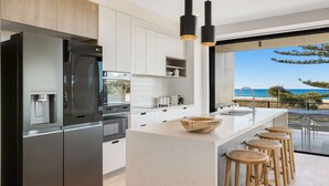 Een moderne keuken met een groot kookeiland, roestvrijstalen apparatuur en uitzicht op het strand.