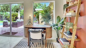 Habitación moderna con escritorio, silla y estantería. Cuenta con un gran ventanal con vistas a un jardín y una piscina.