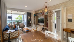 A modern living room with a wooden dining table, comfortable seating, a TV, and a bookshelf. - Apartment Front to the Sea With Barbecue Vdr0202 (Florianópolis)