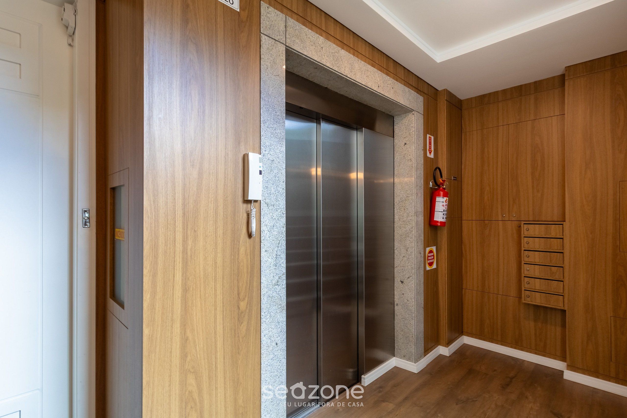 A modern elevator with a metallic finish, flanked by wooden paneling and a fire extinguisher mounted on the wall.