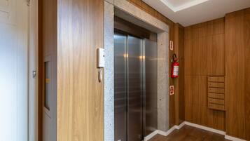 Un ascensor moderno con detalles metálicos, flanqueado por paneles de madera y un extintor de incendios en la pared.