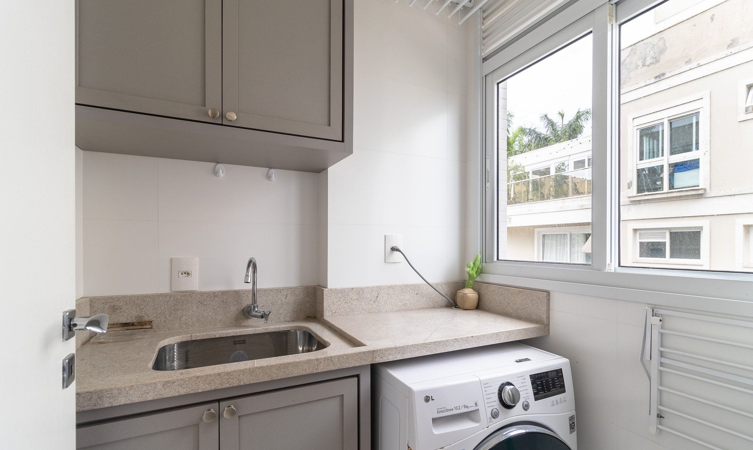Cocina compacta con lavadora integrada, un lavamanos y una ventana con vista a edificios cercanos.