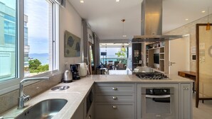 A modern kitchen with a large window, stainless steel appliances, and a view of the sea. - Apartment Front to the Sea With Barbecue Vdr0202 (Florianópolis)