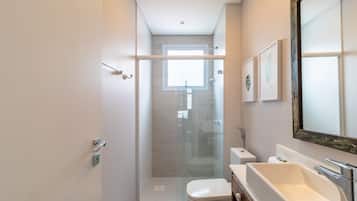 Un baño moderno con cabina de ducha de vidrio, inodoro blanco y un lavamanos grande.