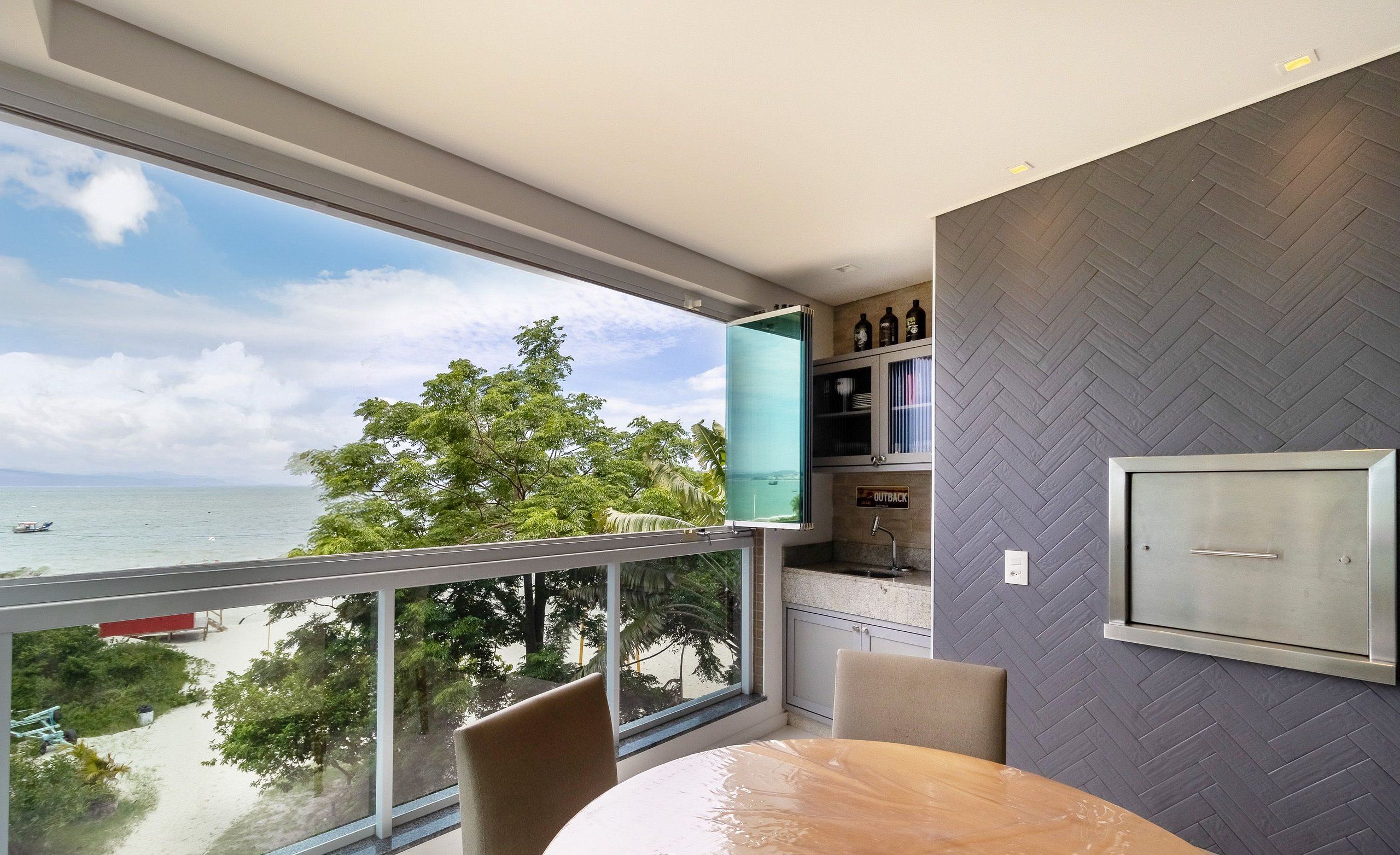 A modern room with a large window overlooking a beach, a round table, and a herringbone-patterned wall.