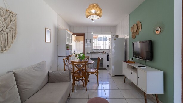 Una sala de estar moderna con sofá, mesa de comedor, sillas, televisor y cocina al fondo.