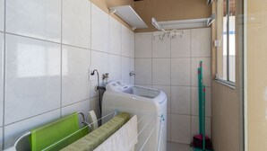 Baño con lavadora, tendedero y escoba.