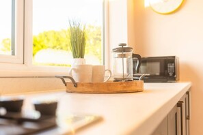 Un comptoir de cuisine avec une machine à café, une casserole et une fenêtre donnant sur un paysage verdoyant.