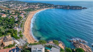 An aerial view of a coastal town with a sandy beach, clear blue waters, and residential buildings.