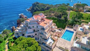 A coastal hotel with multiple balconies, a swimming pool, and lush greenery.