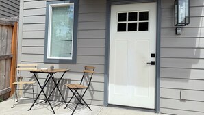 Fachada de una casa con una puerta blanca, una ventana con persianas y una pequeña mesa con sillas.