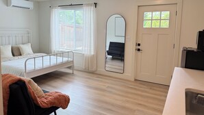 Un dormitorio con cama, una silla, una puerta, un espejo y un equipo de aire acondicionado.