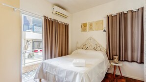 A hotel room with a bed, curtains, a small table with a lamp, and artwork on the wall. - Beautiful Apartments in Canasvieiras - VDM (Florianópolis)