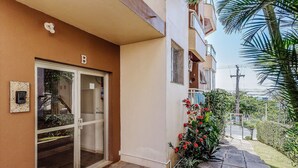 A building entrance with a glass door, a mailbox, and a small garden with red flowers. - Beautiful Apartments in Canasvieiras - VDM (Florianópolis)