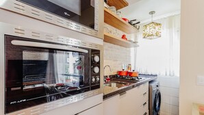 A kitchen with a built-in oven, microwave, and dishwasher, wooden shelves, and a window with curtains. - Beautiful Apartments in Canasvieiras - VDM (Florianópolis)