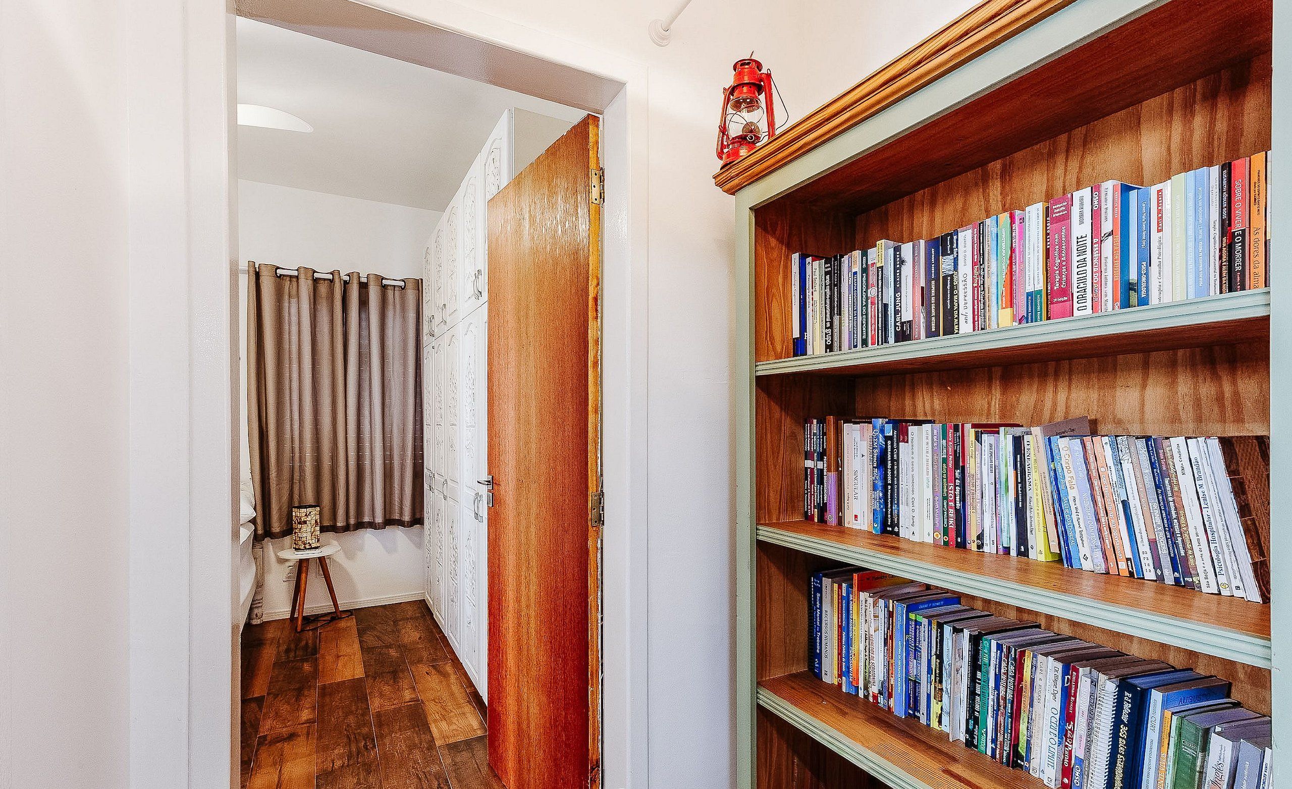 A hallway with a wooden bookshelf filled with books, a small table with a lamp, and a door leading to another room.