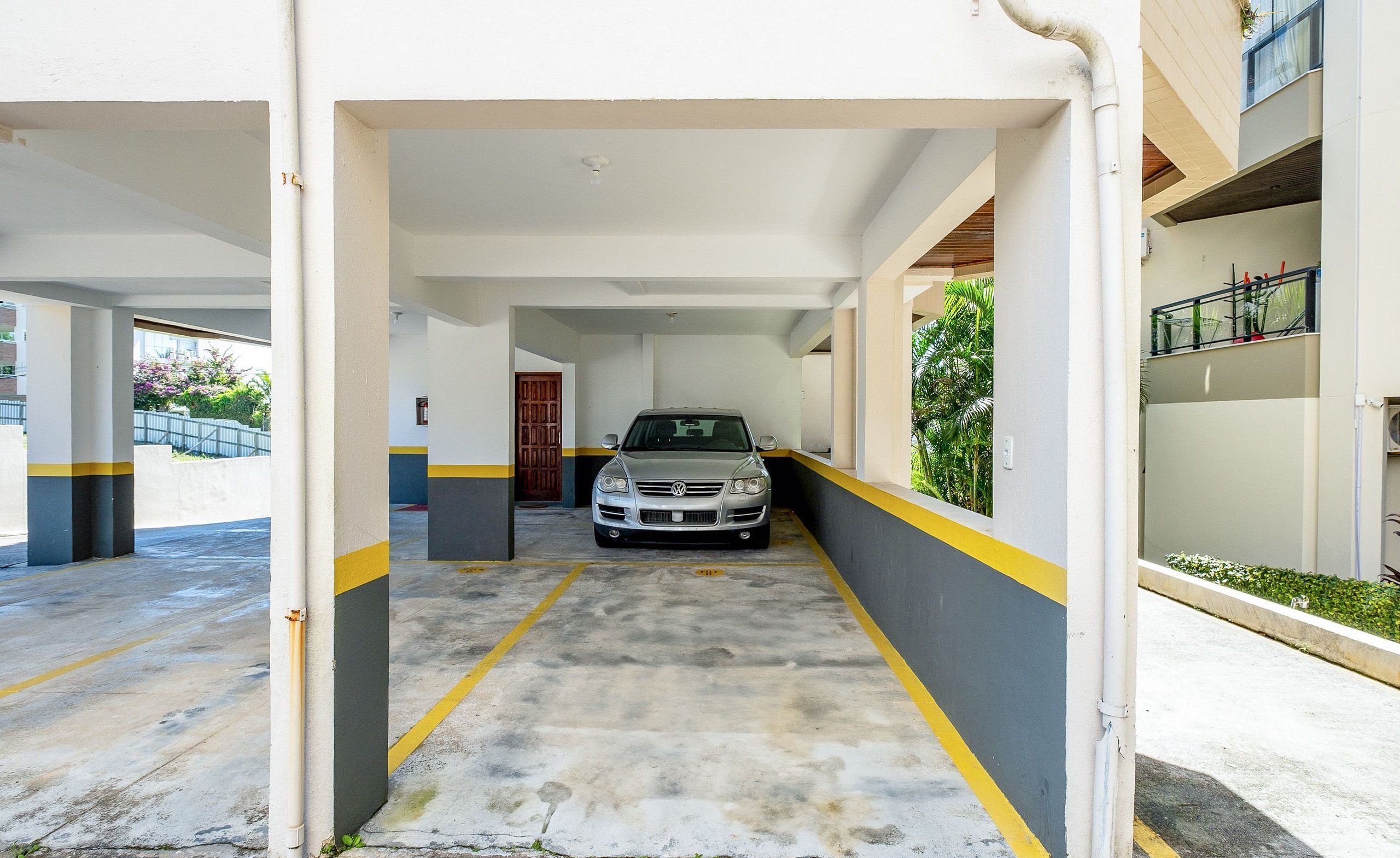 Un estacionamiento con un coche aparcado en el centro, suelo de hormigón y paredes blancas con franjas amarillas.