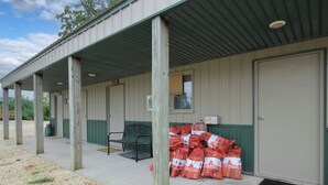 A building with a covered porch, a door, and a window. There are bags of firewood stacked outside. - River Valley Campground (Wadena)