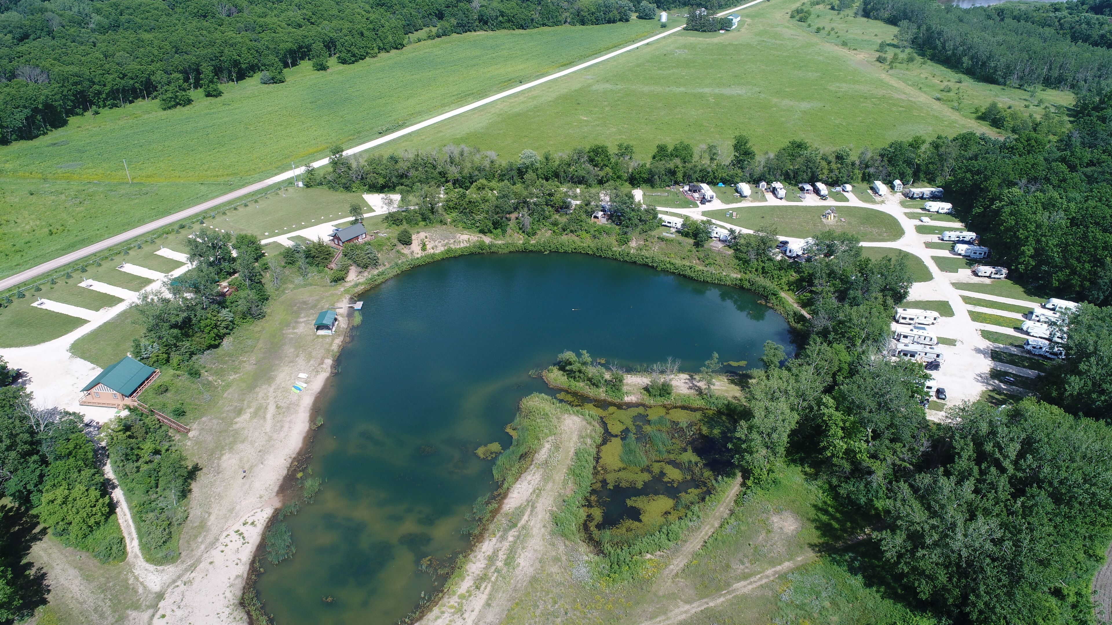 An aerial view of a campsite with a lake, RV parking, and a small building.