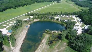 An aerial view of a campsite with a lake, RV parking, and a small building.
