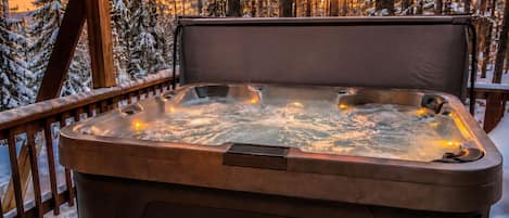 Een hottub op een terras met een besneeuwd bos op de achtergrond.