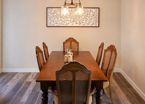 Comedor con mesa de madera, seis sillas, una araña y una obra de arte colgada en la pared.