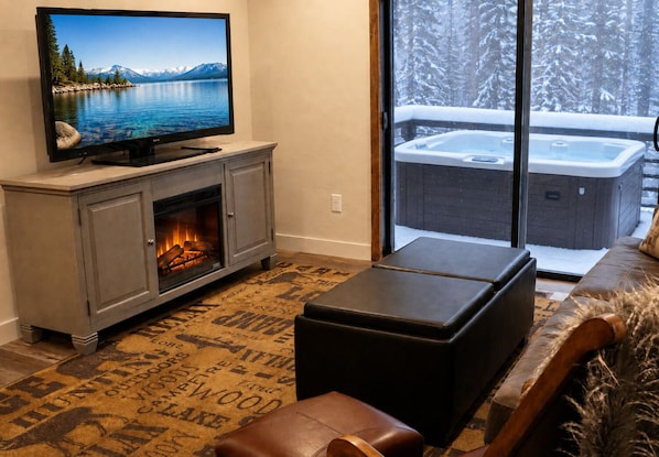 Una sala de estar acogedora con chimenea, televisión y vistas a un jacuzzi exterior.