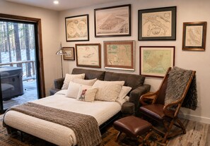 A bedroom with a large bed, a wooden chair, and multiple framed maps on the wall.
