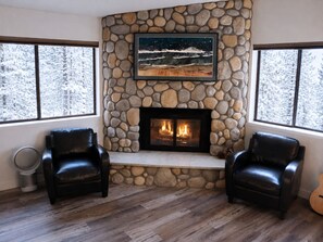 A room with a stone fireplace, two leather chairs, and a guitar.